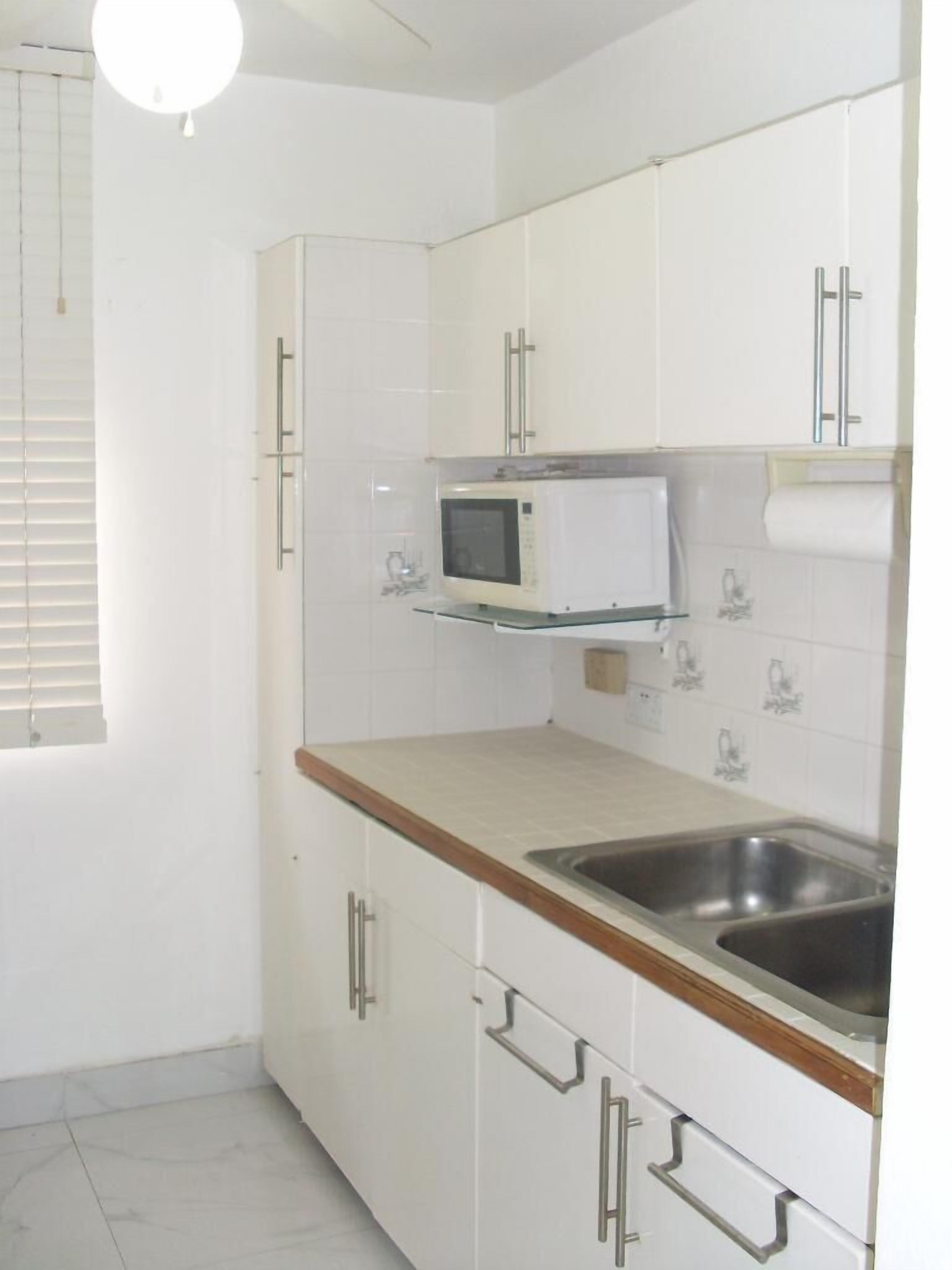A kitchen with white cabinets, a microwave, a sink, and a window with blinds.
