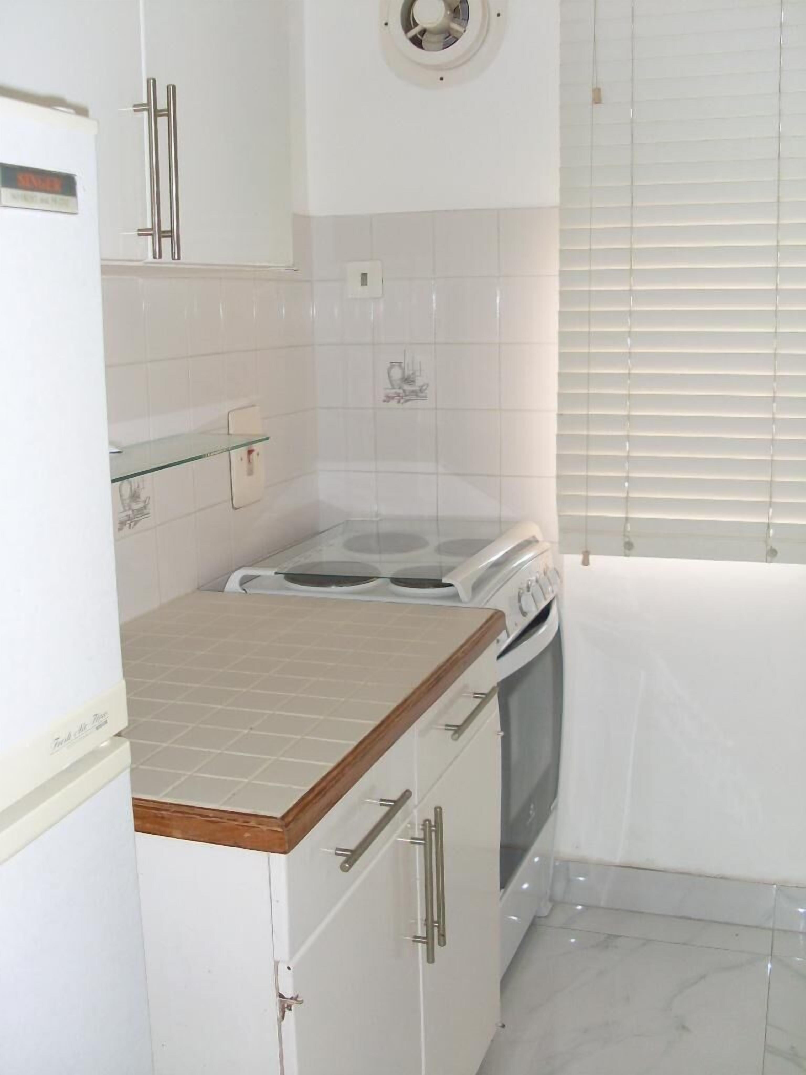 A compact kitchen with white cabinets, a stove, and a refrigerator.