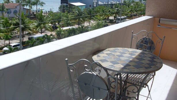 A balcony with a checkered table and chairs, overlooking a coastal area with buildings and palm trees. - Luxurious beach  front self-catering apartment in the heart of Ocho Rios Jamaica (Ocho Rios)