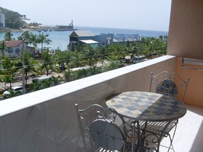 Ein Balkon mit einem karierten Tisch und Stühlen mit Blick auf eine Küstenlandschaft mit Gebäuden und Palmen.
