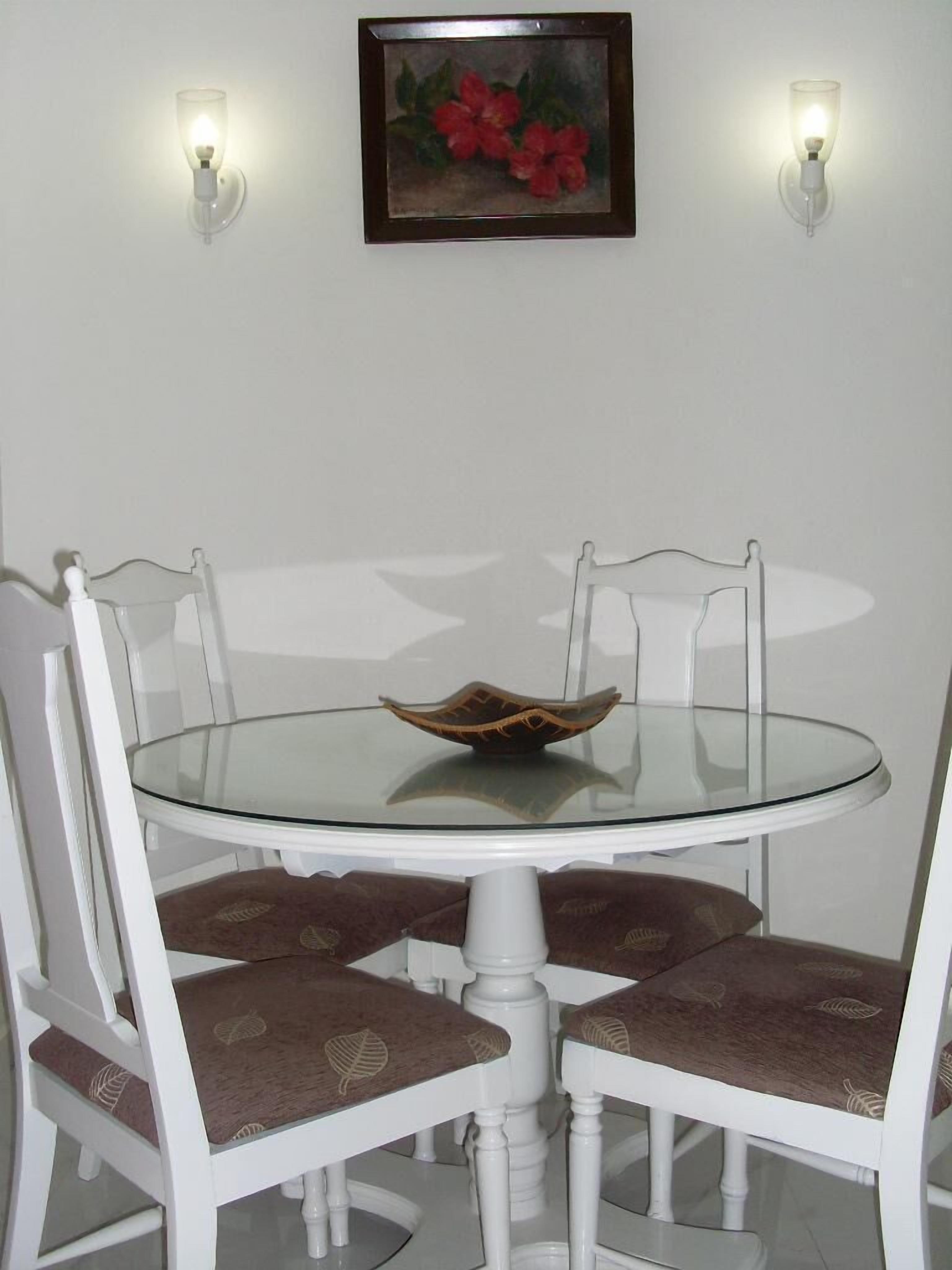 A dining area with a round glass table, four white chairs with brown cushions, and two wall-mounted lights.