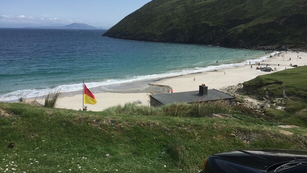 A coastal beach with a flag, grassy areas, and a clear view of the sea.