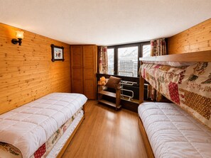 Quarto com duas camas de solteiro, um guarda-roupa de madeira, janela com cortinas e uma pequena mesa de cabeceira com abajur.