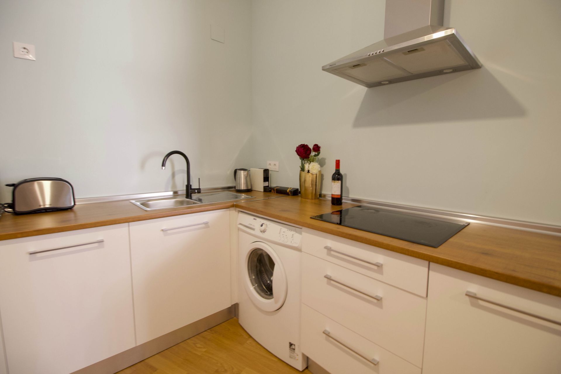 Cocina compacta con lavadora, tostadora, pileta y campana extractora de acero inoxidable.