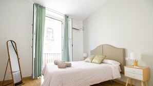 A bedroom with a bed, a nightstand, a lamp, a mirror, and a window with curtains. - Tetuán 2D - Two Bedroom Apartment, Sleeps 4 (Sevilla)