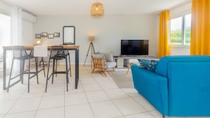 Una sala de estar moderna con sofá, televisor, zona de comedor y balcón con cortinas amarillas.