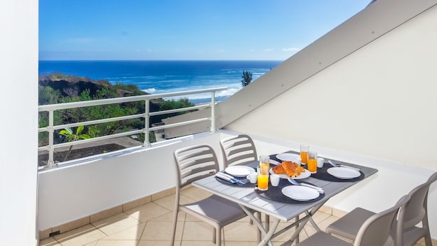Un balcón con una mesa lista para el desayuno, con vista al océano.