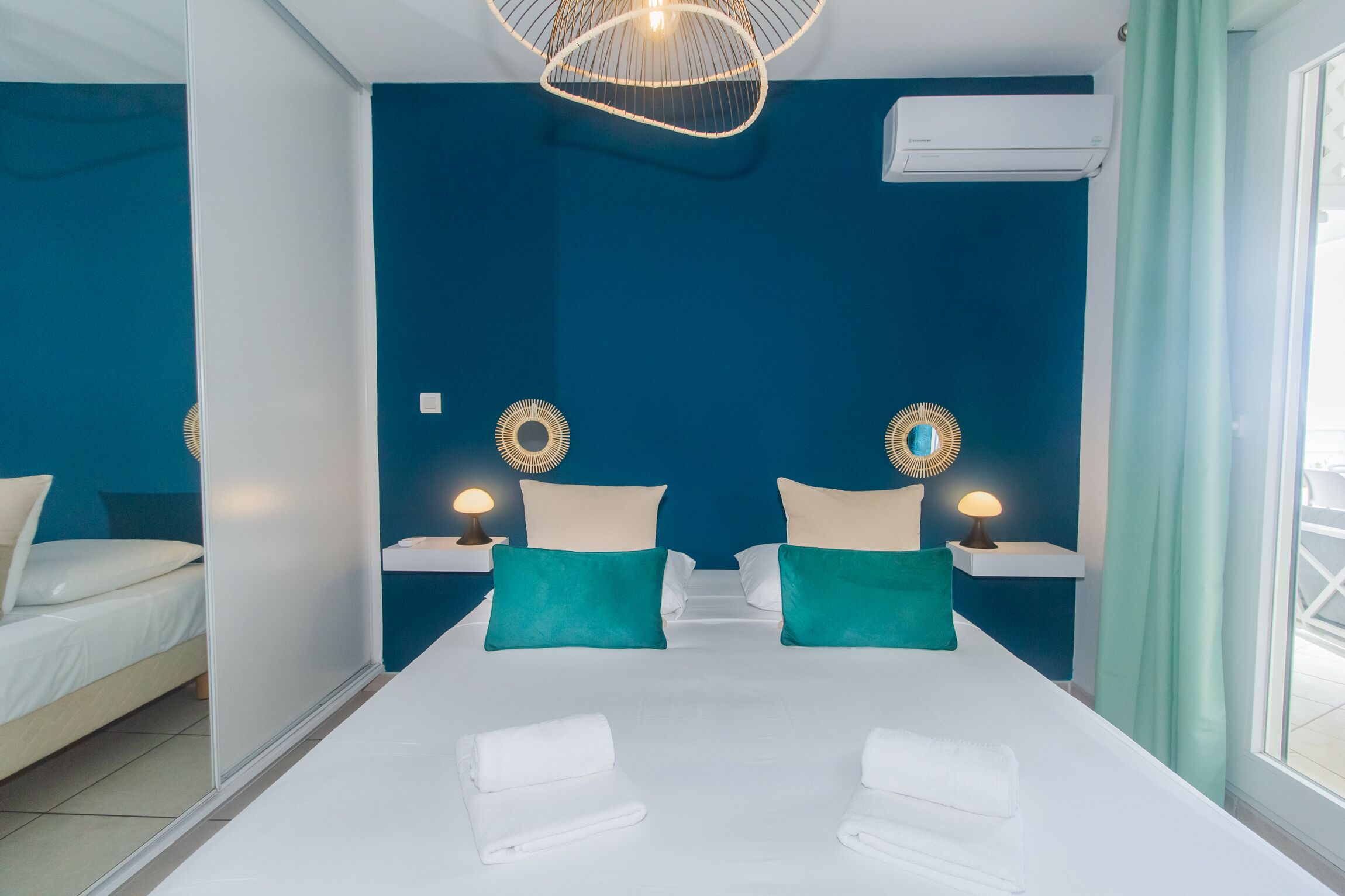 Habitación de hotel con una cama grande, dos mesitas de noche con lámparas, un candelabro y un equipo de aire acondicionado.