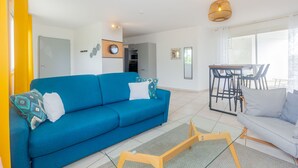 Una sala de estar moderna con un sofá azul, un comedor con mesa y sillas, y un ventanal que proporciona luz natural.
