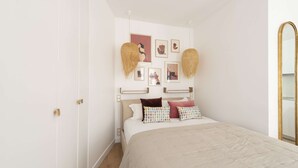 A bedroom with a bed, white walls, and a gold-framed mirror. - Candide, Studio, 2 people (París)