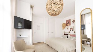 A bedroom with a bed, a chair, a TV, a mirror, and a hanging light fixture. - Candide, Studio, 2 people (París)
