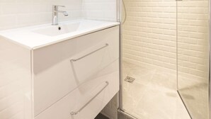 A modern bathroom with a white vanity, a large mirror, and a glass-enclosed shower. - Candide, Studio, 2 people (París)