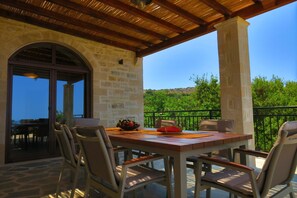 An outdoor patio with a table set for two, surrounded by chairs, and a view of greenery and hills in the background.