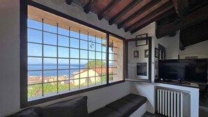 Habitación con un gran ventanal que da a vistas costeras, un sofá negro, un televisor y un radiador.