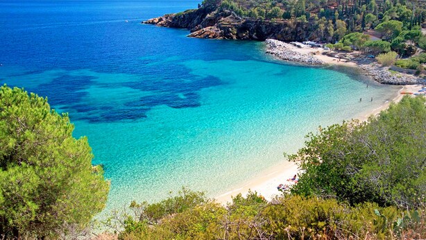 Un paisaje costero con aguas azul turquesa, una playa arenosa y un litoral rocoso.