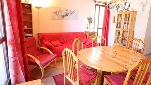 A cozy living room with a red sofa, wooden chairs, a round wooden table, and a bookshelf. - Cozy Mountain Apartment - Sleeps 6, 2 Balconies, Near Slopes - Arêches-Beaufort (Arêches-Beaufort)