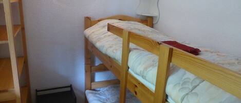 A bunk bed room with a ladder, a small desk, and a wall-mounted lamp.