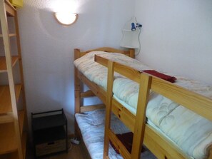 Quarto com beliche, uma escrivaninha pequena e uma luminária fixada na parede.