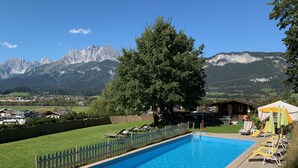 A swimming pool with a view of mountains, a large tree, and a wooden cabin.