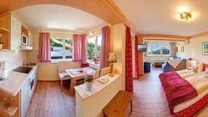 A cozy room with a bed, a desk, a chair, a small table, and a window with curtains.