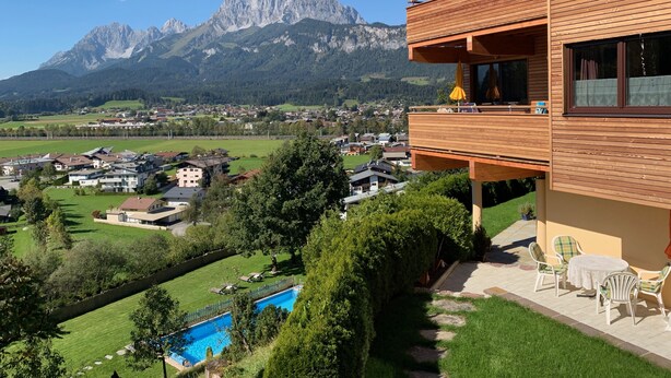 A modern wooden building with a balcony overlooking a swimming pool and a mountainous landscape.