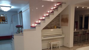 A modern living room with a white sofa, a round coffee table, a piano, and a staircase with illuminated steps. - Beautiful holiday home in Paris (Paray-Vieille-Poste)