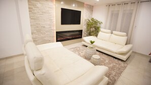 A modern living room with a white sofa, a flat-screen TV mounted on the wall, and a fireplace. - Beautiful holiday home in Paris (Paray-Vieille-Poste)