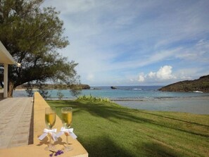 A table with two glasses of champagne and a flower, overlooking a body of water and a grassy area. - Romantic Beachfront Paradise Villa with Incredible Ocean Views & Outdoor Event Space (Islote Arecibo)