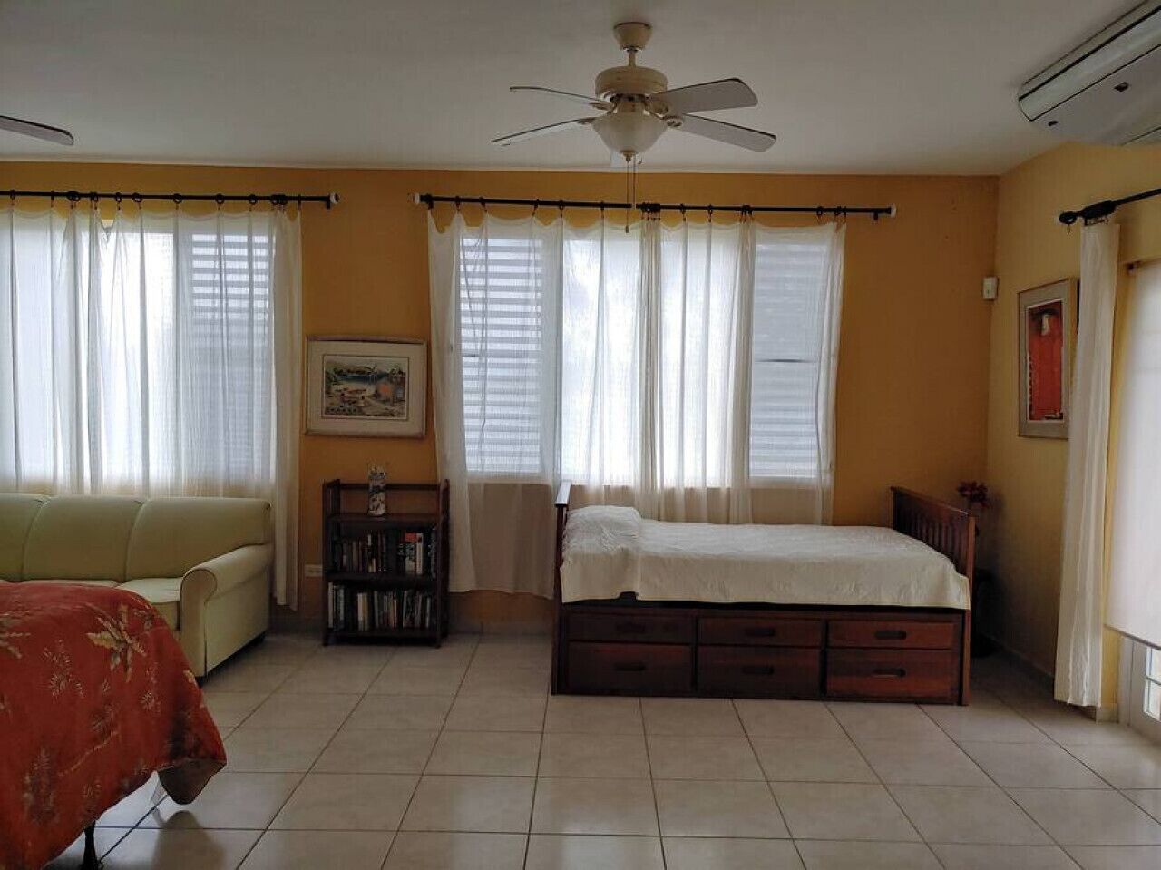 Ein Schlafzimmer mit einem Bett, einem Sofa, einem Deckenventilator und einem Bücherregal.