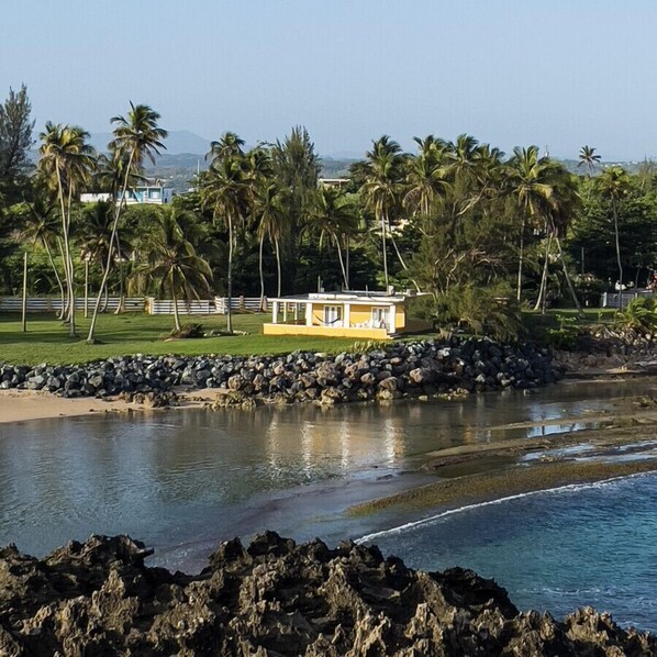 A coastal property with a small yellow building, palm trees, and a rocky shoreline. - Romantic Beachfront Paradise Villa with Incredible Ocean Views & Outdoor Event Space (Islote Arecibo)