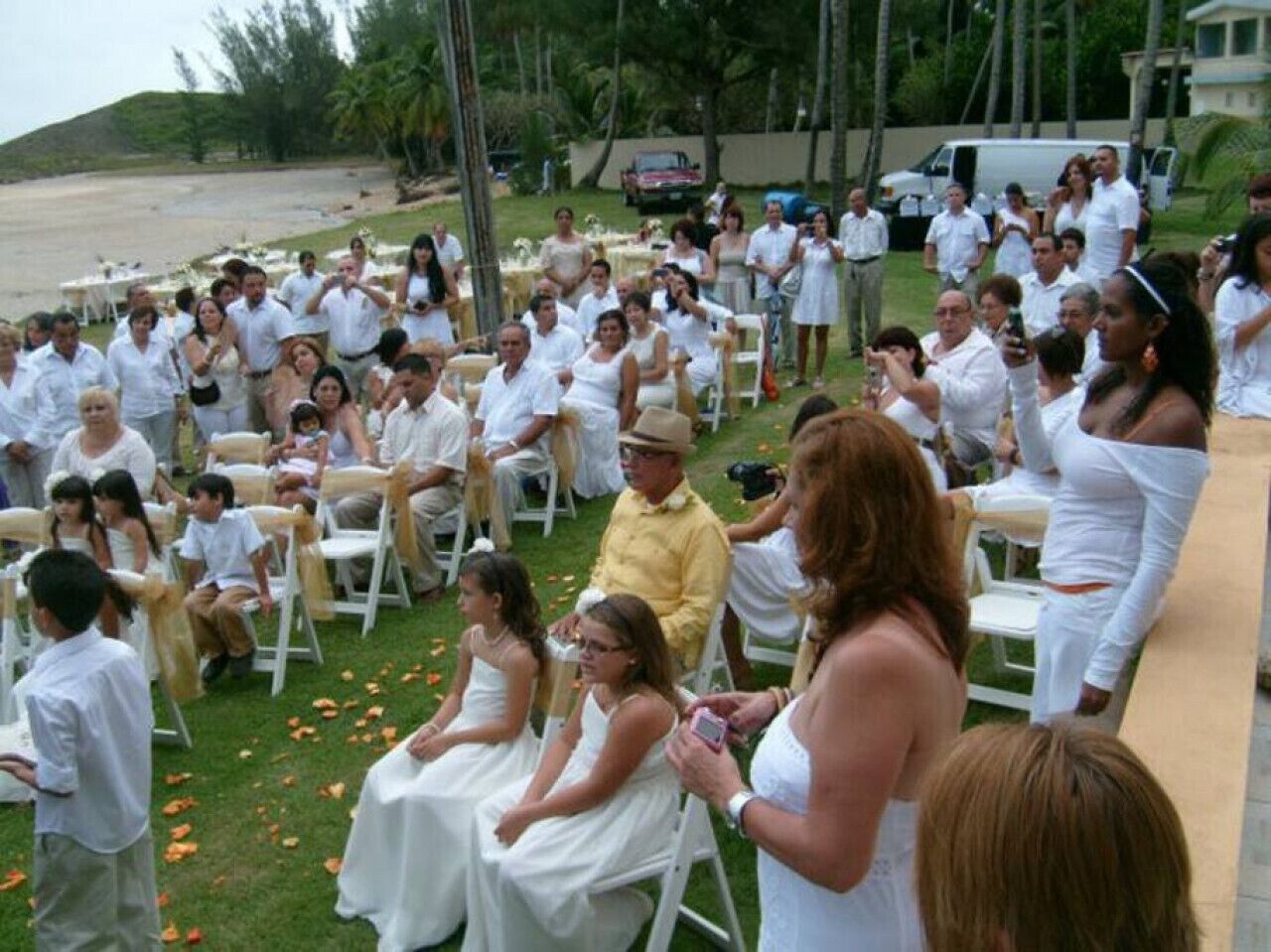 Ceremonia de boda al aire libre con invitados sentados en sillas blancas dispuestas en filas.