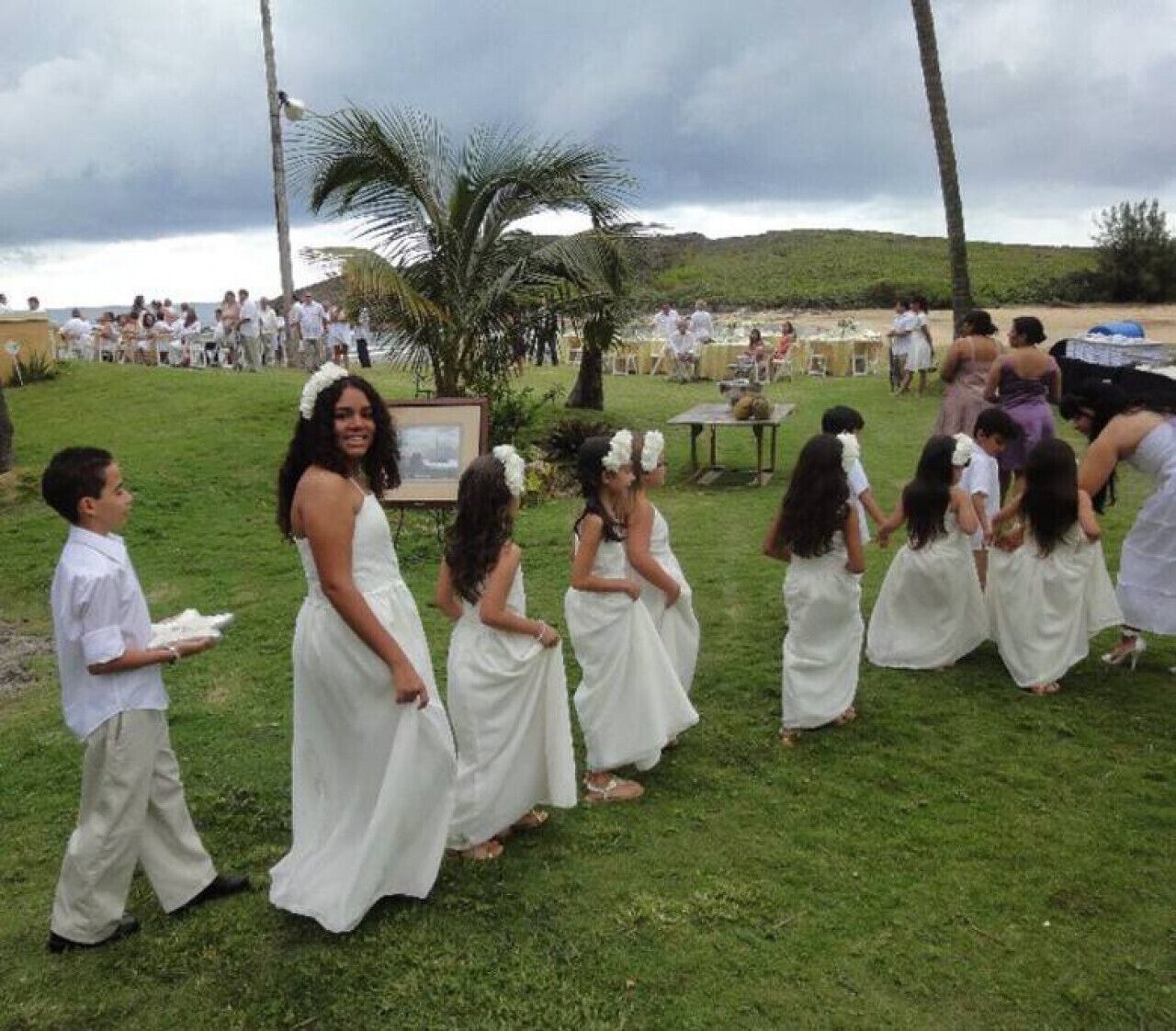 A wedding ceremony outdoors with guests and children in white attire.