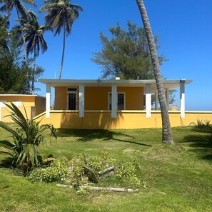 A yellow building with a white porch and a small garden area with palm trees and shrubs. - Romantic Beachfront Paradise Villa with Incredible Ocean Views & Outdoor Event Space (Islote Arecibo)