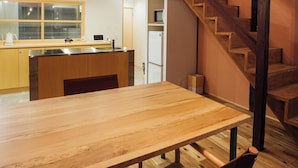 A spacious dining area with a wooden table and chairs, a kitchen in the background, and a wooden staircase. - MINKA Riverside Villas (Imizu)