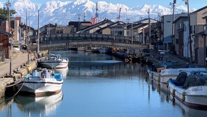 A canal with boats docked, a bridge, and snow-capped mountains in the background. - MINKA Riverside Villas (Imizu)