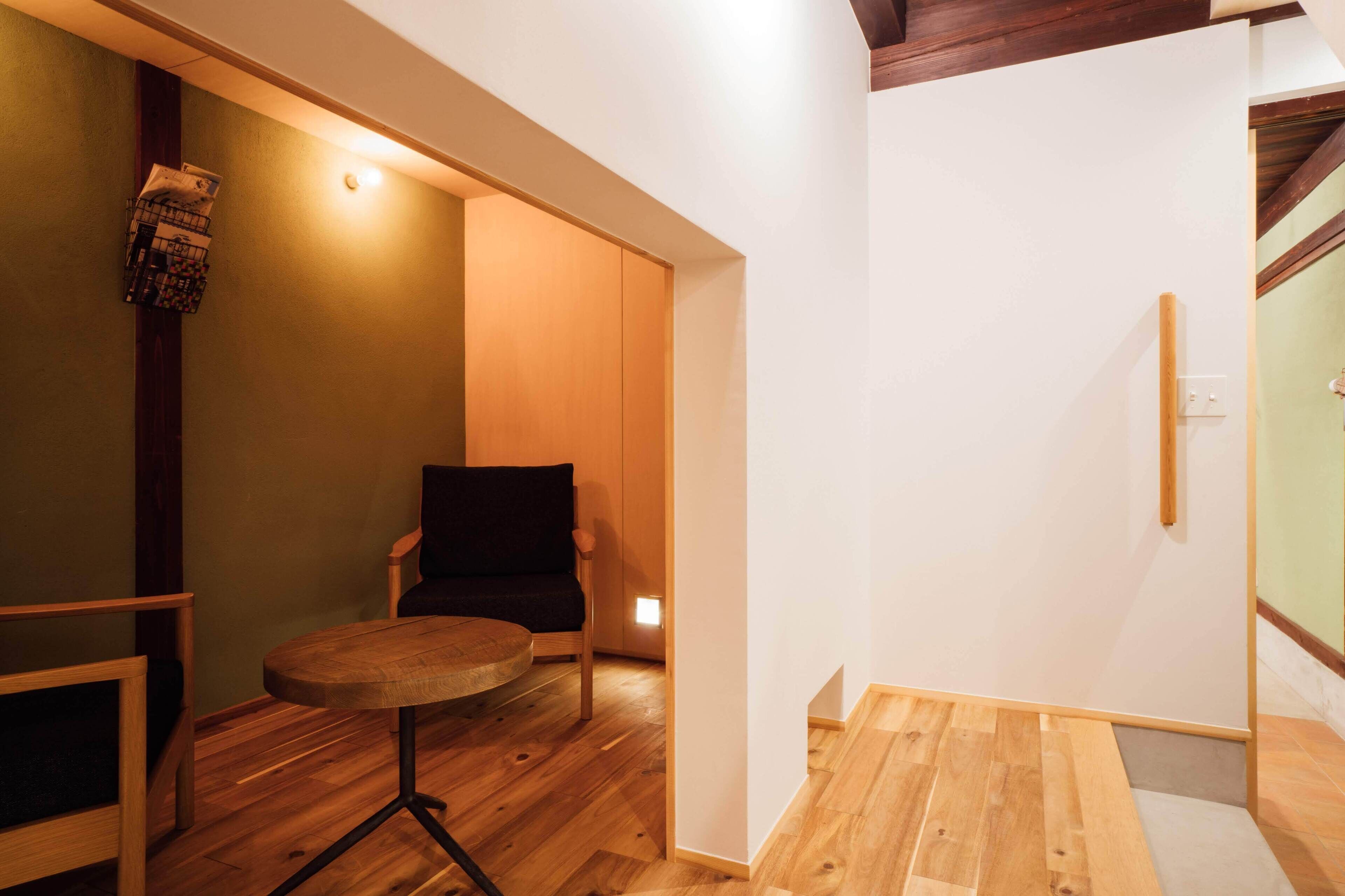 Une pièce avec un plancher en bois, une table ronde, une chaise noire et une petite étagère avec des magazines.