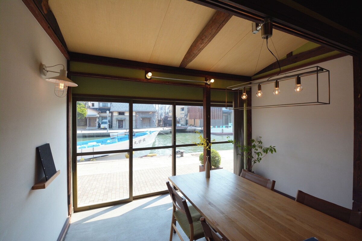 A spacious dining area with a large table, chairs, and a view of a water body outside.