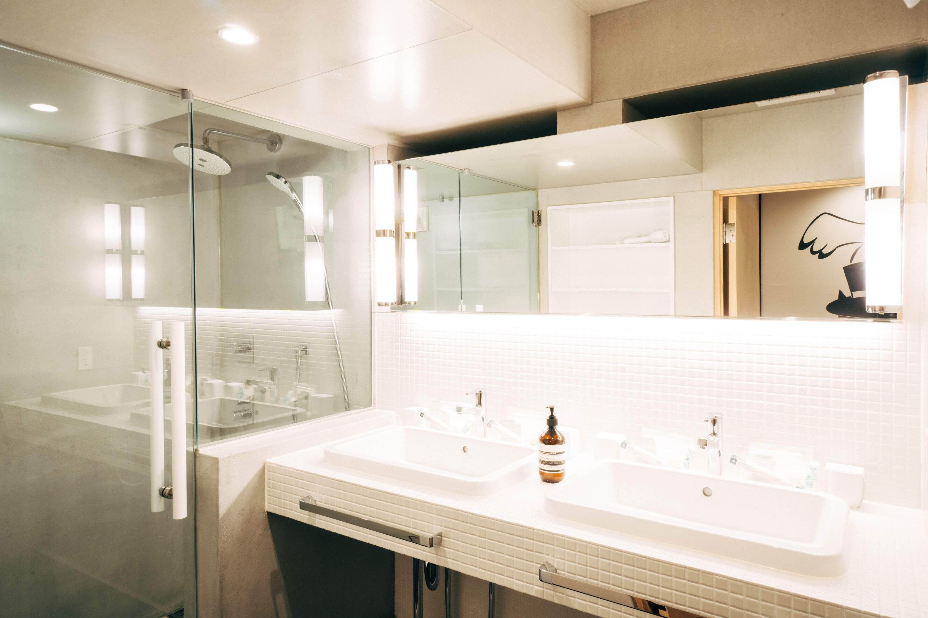 A modern bathroom with two sinks, a glass shower enclosure, and a large mirror.