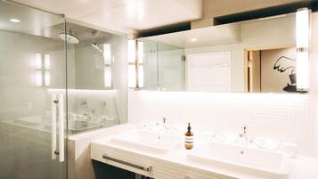 A modern bathroom with two sinks, a glass shower enclosure, and a large mirror.