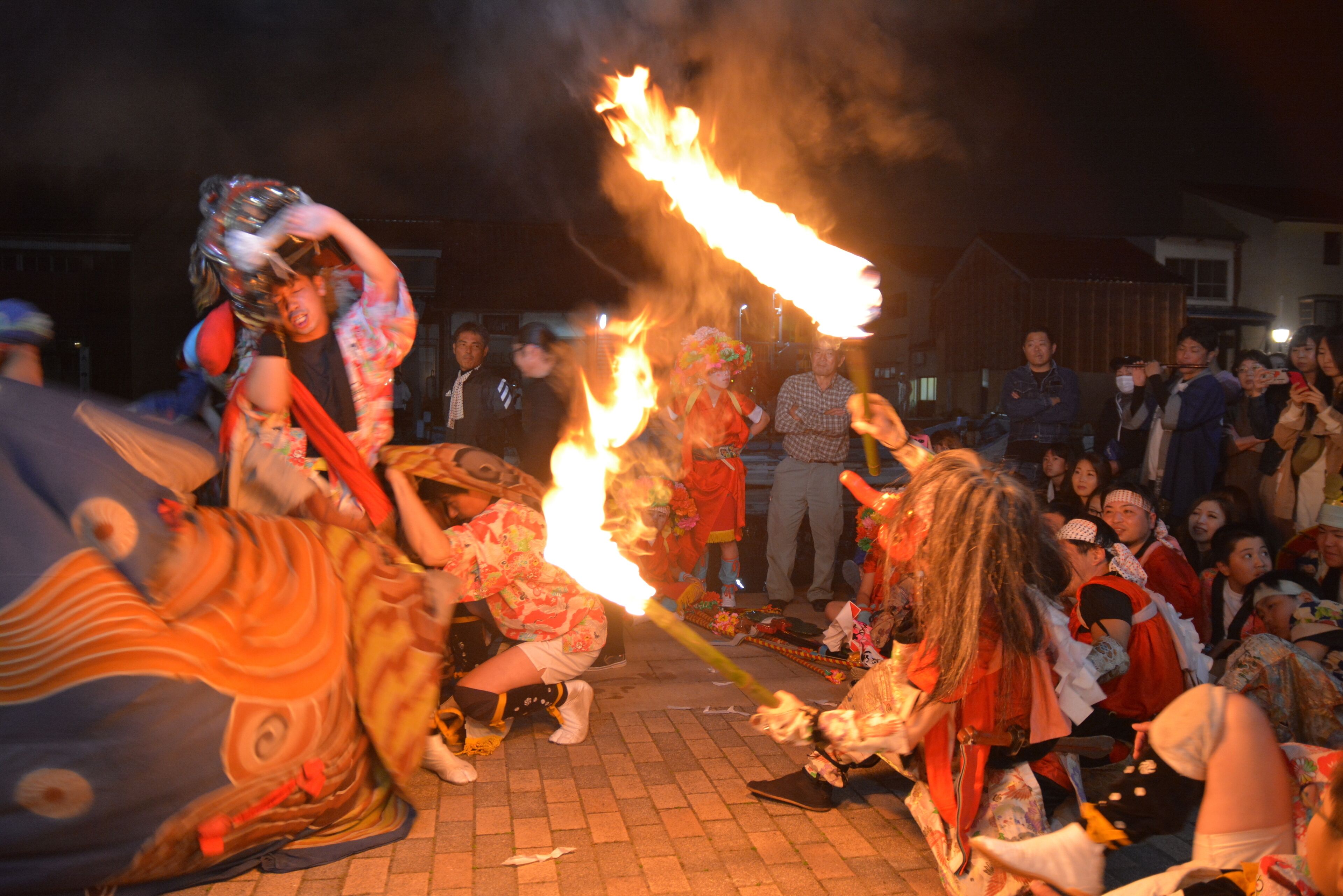 A group of people performing a traditional fire dance with torches, surrounded by an audience.