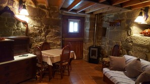 A stone-walled room with a wooden table and chairs, a sofa, and a fireplace.