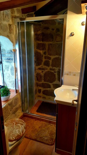 A bathroom with a stone wall, a shower, a sink, and a patterned rug.