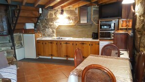 Uma cozinha rústica com armários de madeira, parede de pedra e um espaço de refeições com mesa e cadeiras.