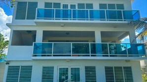 A two-story building with a balcony on the second floor, multiple windows with shutters, and outdoor seating. - Luquillo Beachfront Villa with Ocean Views & Room to Relax (Luquillo)