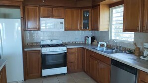 A kitchen with wooden cabinets, a stove, a dishwasher, and a window. - Luquillo Beachfront Villa with Ocean Views & Room to Relax (Luquillo)