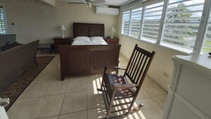 A bedroom with a bed, a chair, a desk, a ceiling fan, and a window with blinds. - Luquillo Beachfront Villa with Ocean Views & Room to Relax (Luquillo)