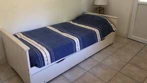 A single-bed room with a white frame, a blue and white striped bedspread, a bedside lamp, and a framed picture on the wall. - Le relais de la Sicarde (Saint-Denis-d´Oléron)