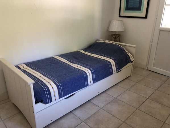 A single-bed room with a white frame, a blue and white striped bedspread, a bedside lamp, and a framed picture on the wall.