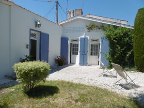 A building with a gravel driveway, a small garden with a bush, and a folding chair.