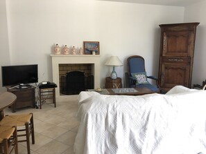 Un salon avec une cheminée, un téléviseur, un fauteuil bleu et un meuble en bois.